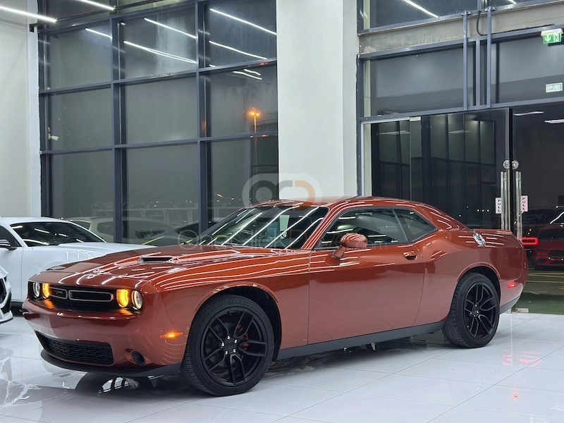 Front three-quarter view of an orange Dodge Challenger muscle car, available as a car for sale in Dubai at a low price.
